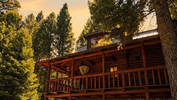 A wooden cabin with a stone foundation, surrounded by trees and a clear sky.