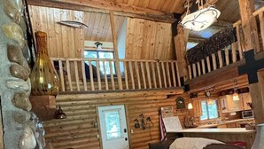 A log cabin interior with a stone wall, a wooden ceiling, a sofa, a dining area, and a staircase. - Sagebrush Meadows+Hotub+WiFi+20minsYellowstone (Island Park)
