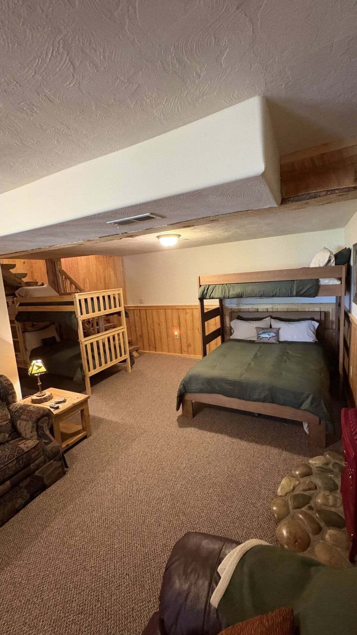 A room with bunk beds, a wooden wardrobe, a small table with a lamp, and a couch.