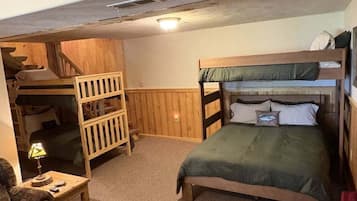 A room with bunk beds, a wooden wardrobe, a small table with a lamp, and a couch.
