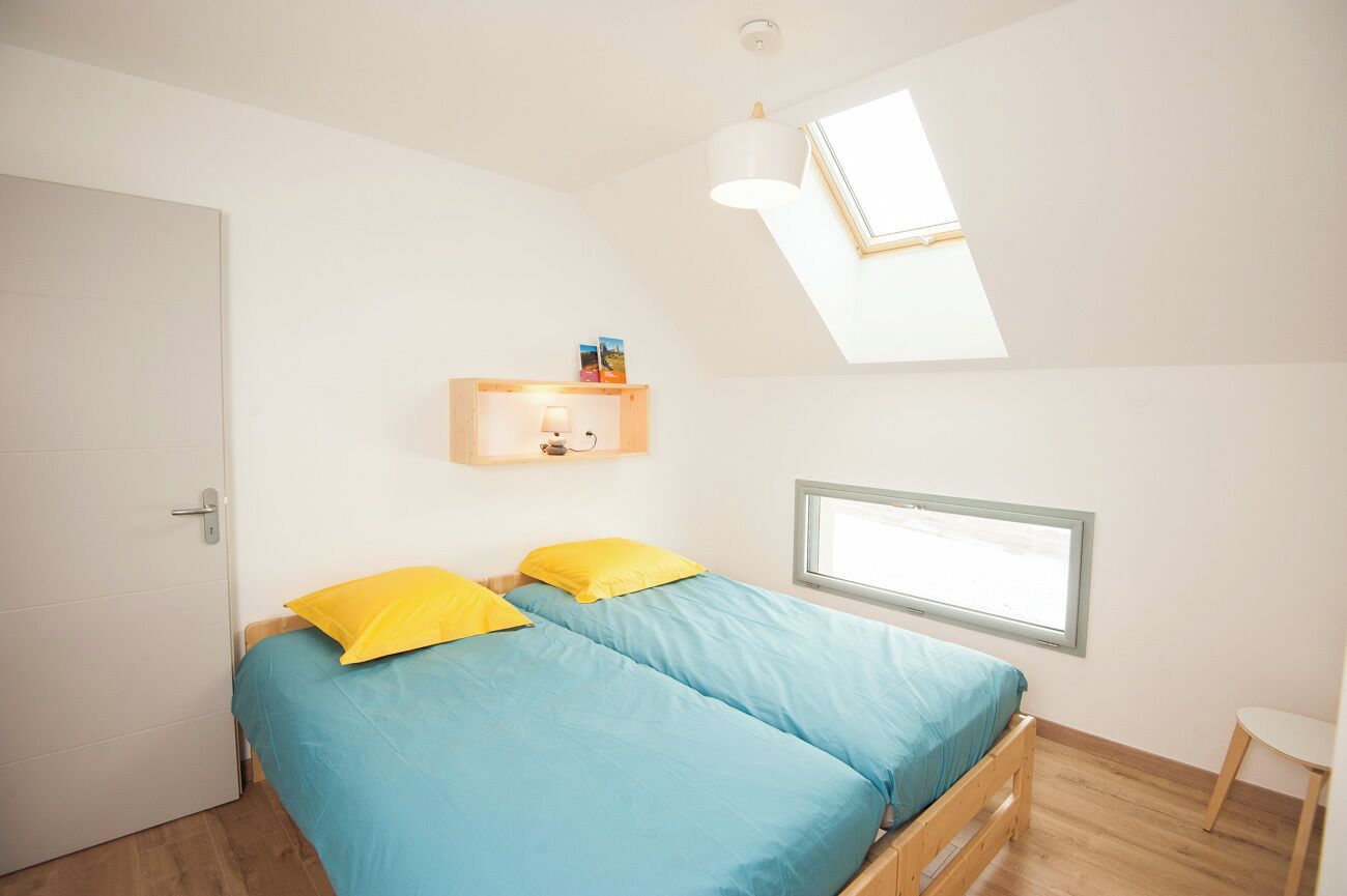 A bedroom with two beds, a skylight, a window, and a small table.