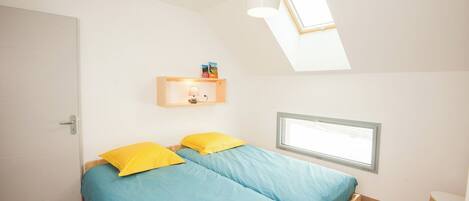 A bedroom with two beds, a skylight, a window, and a small table.