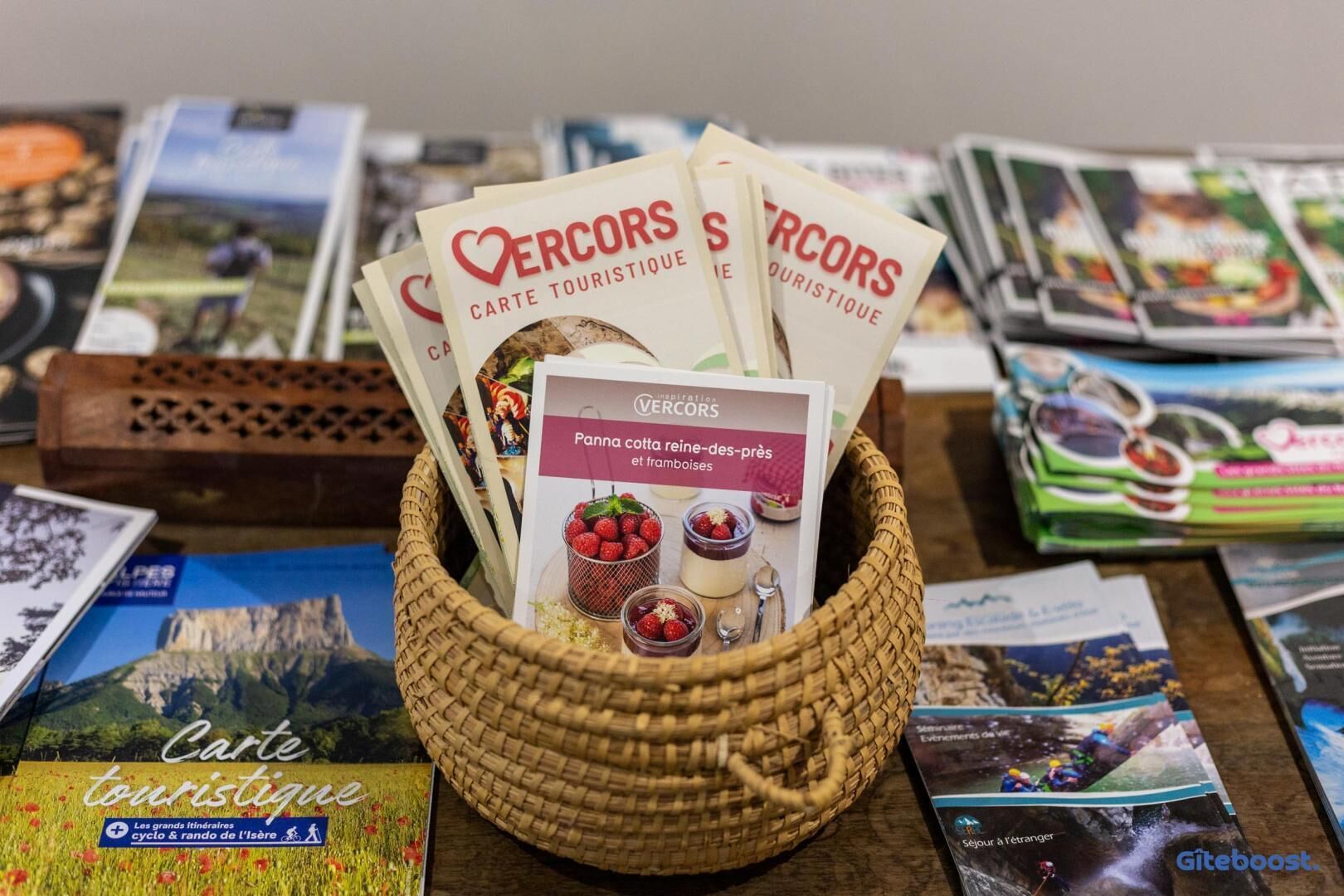 Una cesta con folletos y una tarjeta con el texto 'ERCORS CARTE TOURISTIQUE' y 'Panna cotta reine-des-près y framboises'.