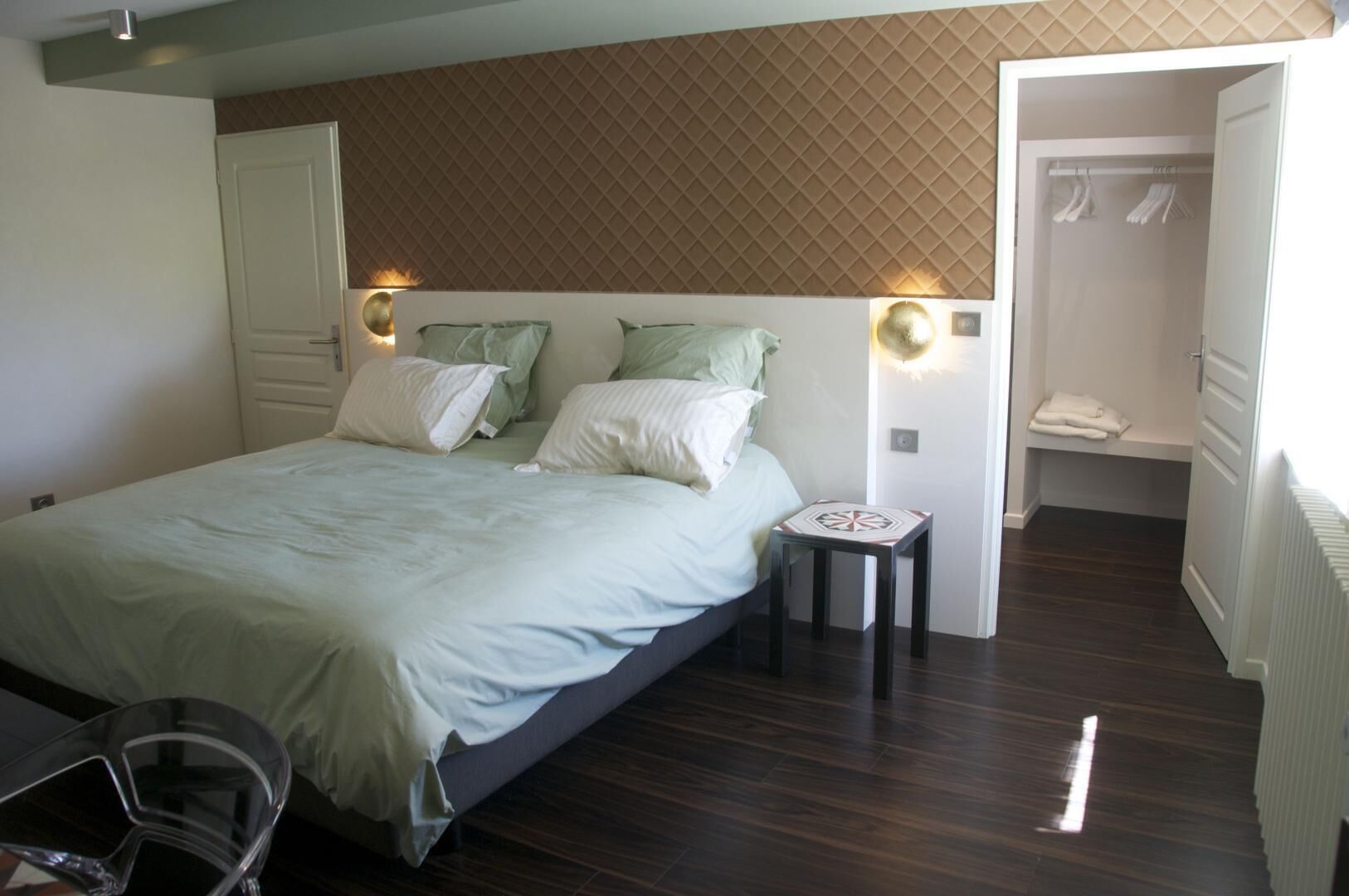 Un dormitorio con cama, lámparas de noche, una mesita y un vestidor.