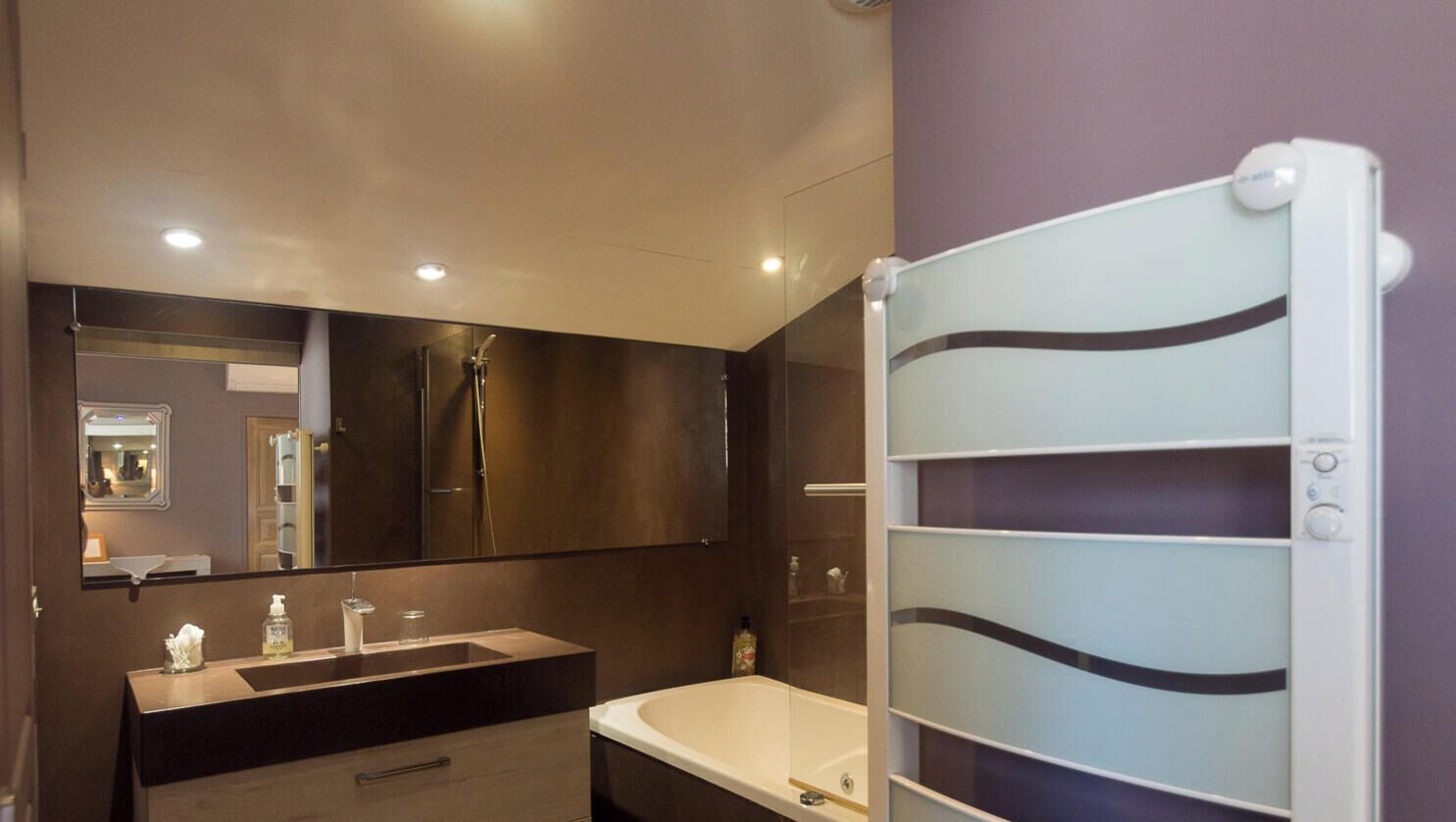 Une salle de bain moderne avec un grand miroir, une baignoire et un espace douche.