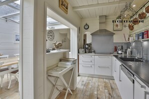 Ett kök med vita köksskåp, en diskho i rostfritt stål och en hängande hylla för kastruller.