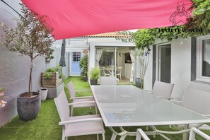 Eine Terrasse mit einem Glastisch und weißen Stühlen, umgeben von Kübelpflanzen und einem pinkfarbenen Baldachin.