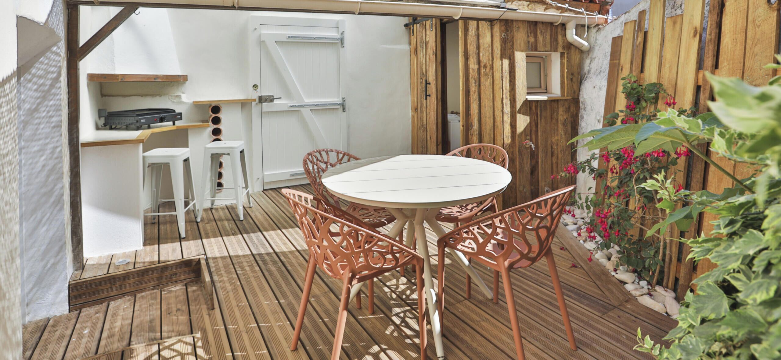 An outdoor patio with a round table and chairs, a white door, and a wooden fence.