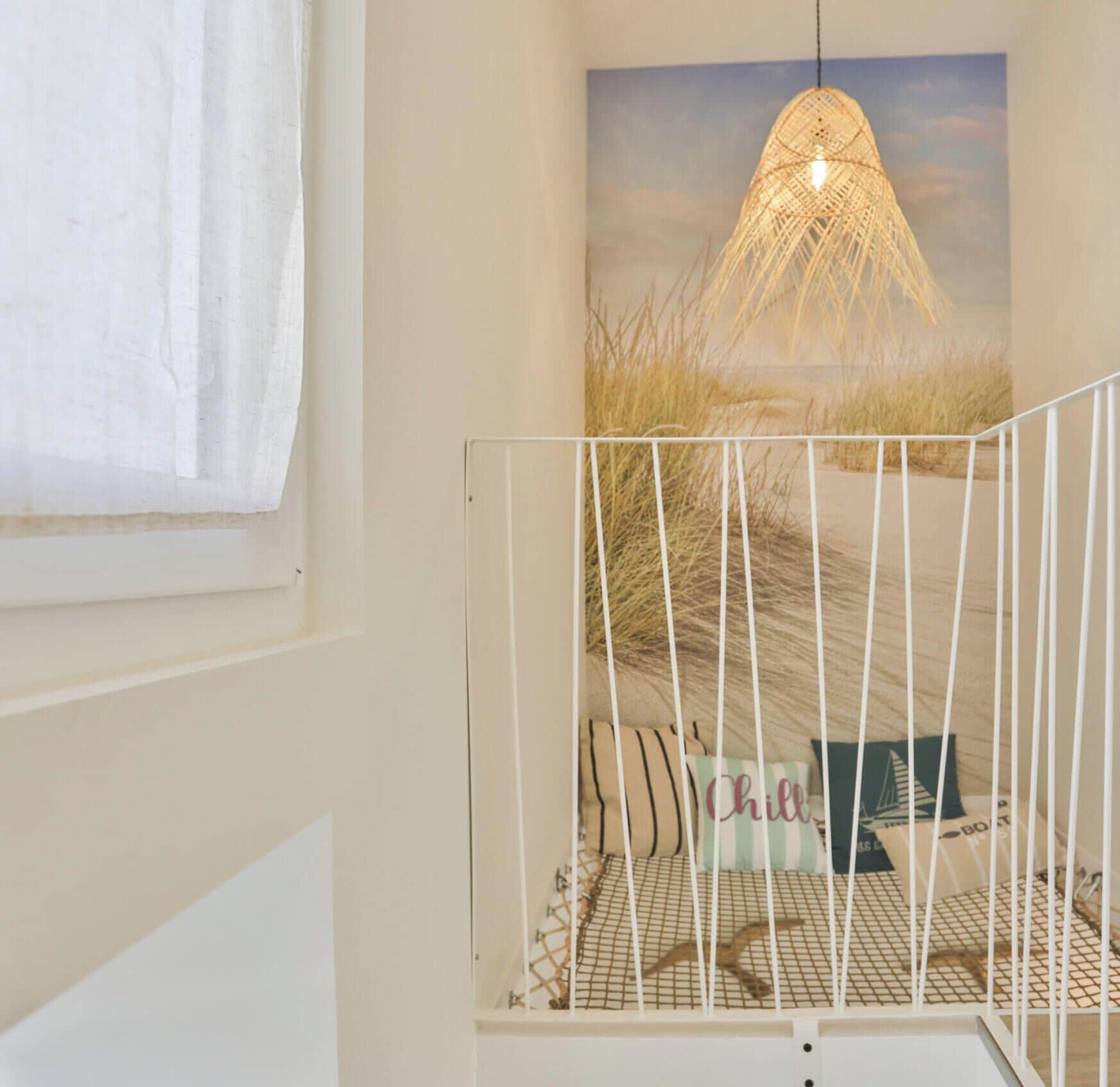 A staircase with a white railing, a wall-mounted light fixture, and a painting of a beach scene.