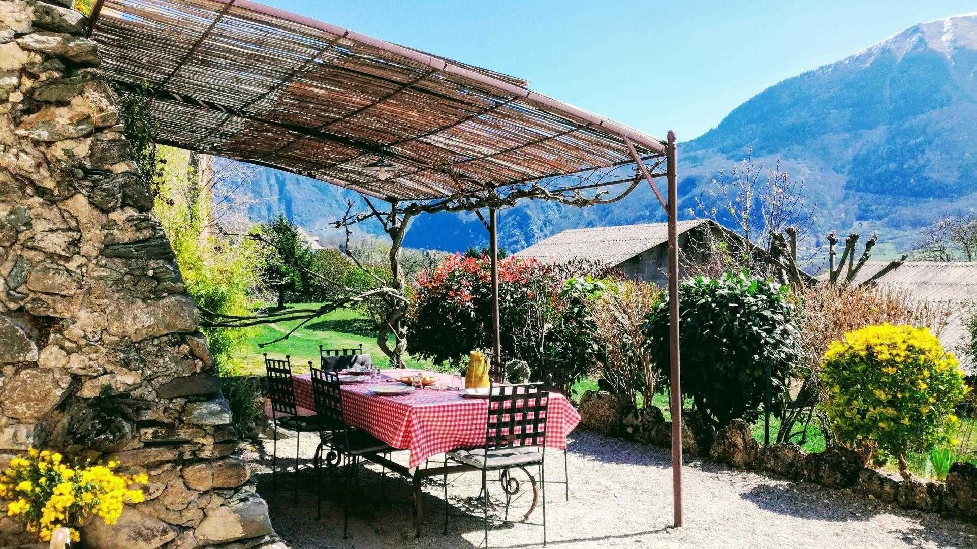 Un bâtiment en pierre doté d’un patio couvert, une table recouverte d’une nappe à carreaux et une vue sur les montagnes.