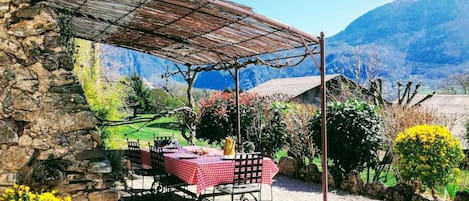 Un bâtiment en pierre doté d’un patio couvert, une table recouverte d’une nappe à carreaux et une vue sur les montagnes.