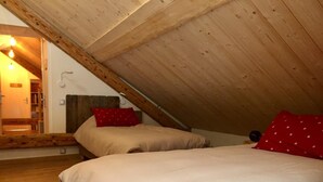 A bedroom with a sloped ceiling, wooden beams, a bed with white bedding, and a red pillow. - Le Nid in Chartreuse (SAINT PIERRE DE CHARTREUSE)