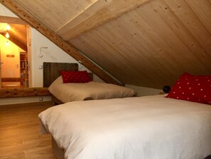 A bedroom with a sloped ceiling, wooden beams, a bed with white bedding, and a red pillow. - Le Nid in Chartreuse (SAINT PIERRE DE CHARTREUSE)