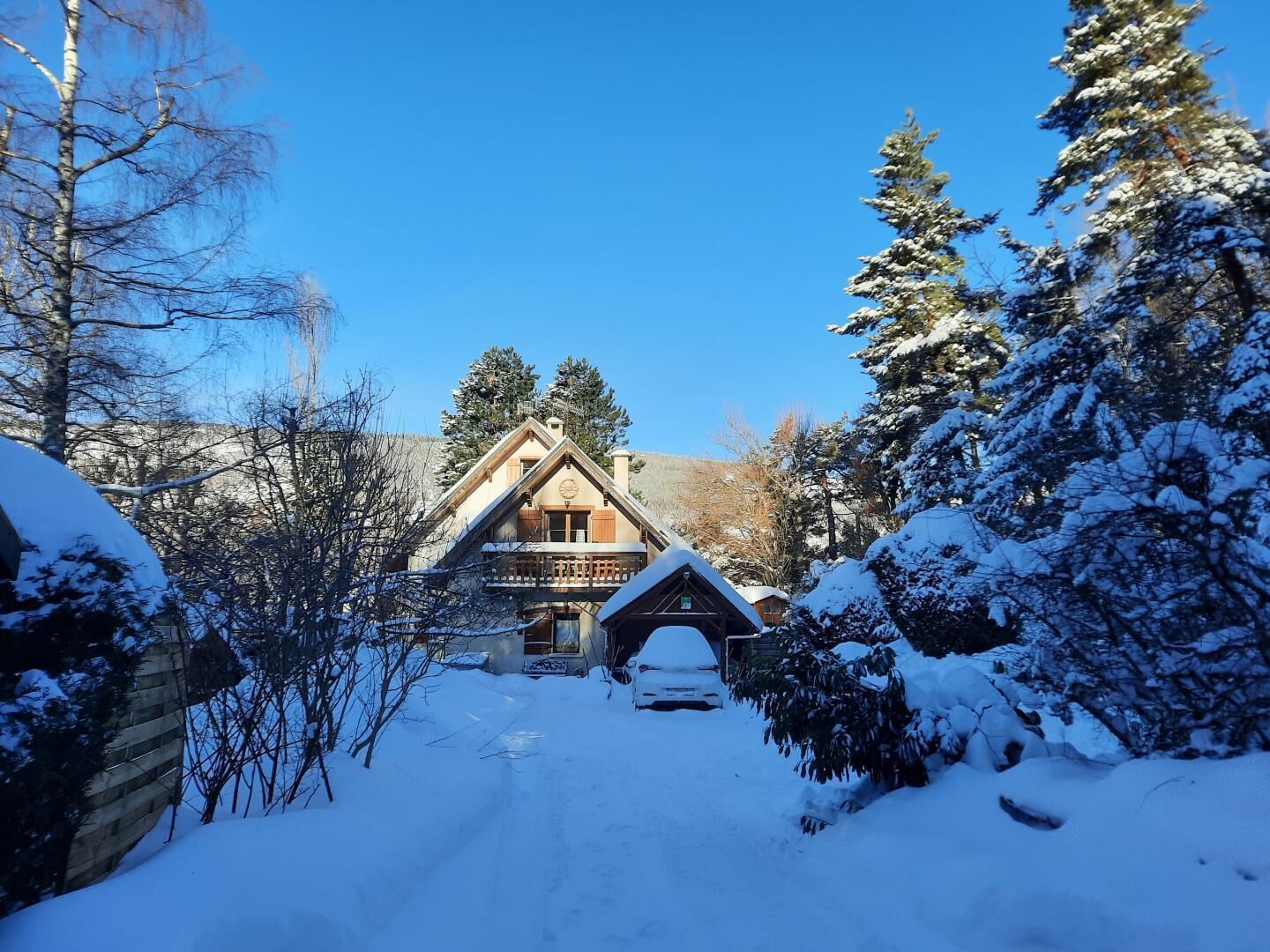 Una cabaña de madera con techo pronunciado, rodeada de árboles cubiertos de nieve y un cielo azul despejado.
