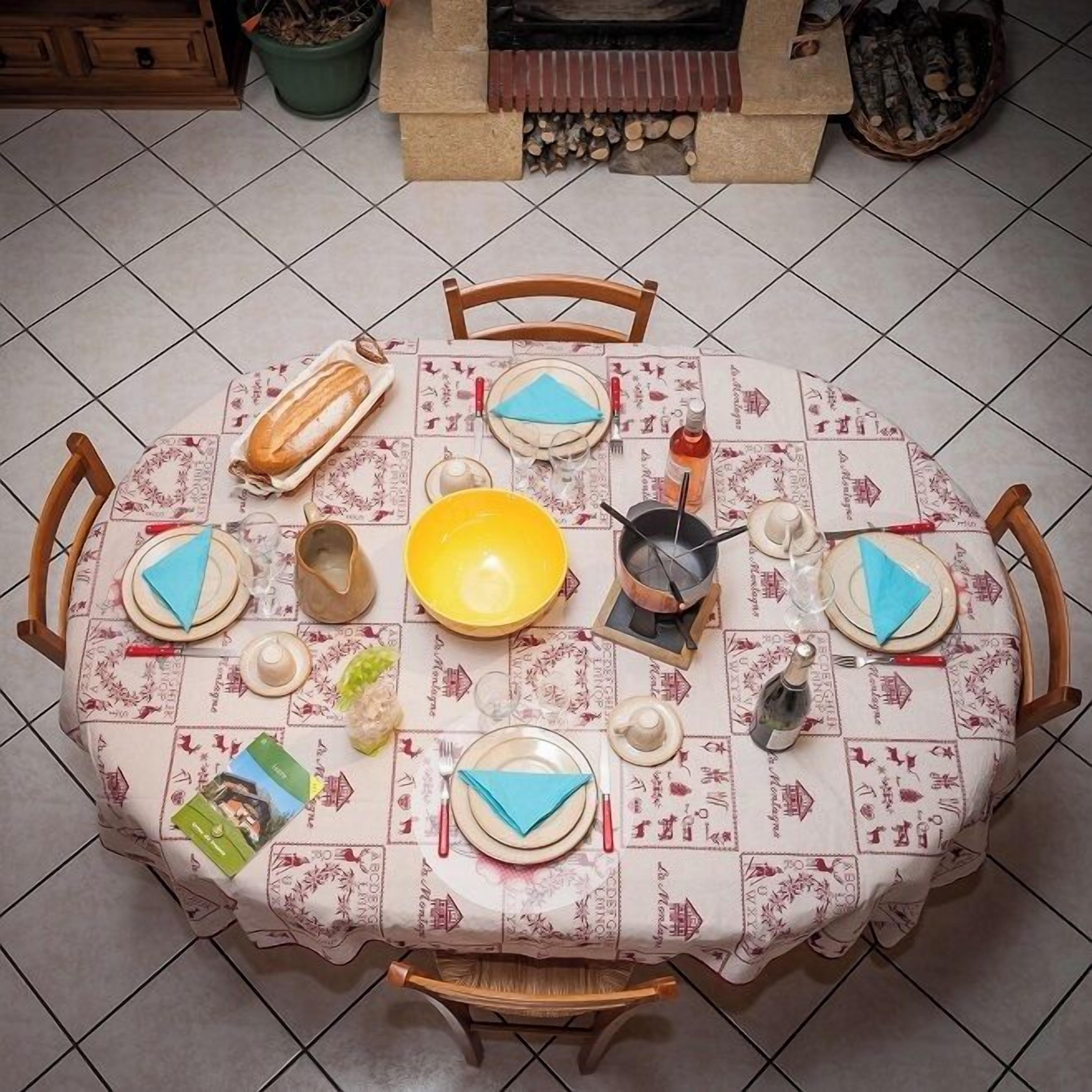 Une table de salle à manger ronde, recouverte d’une nappe à motifs, entourée de chaises en bois.