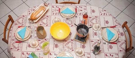 A round dining table with a patterned tablecloth, surrounded by wooden chairs.