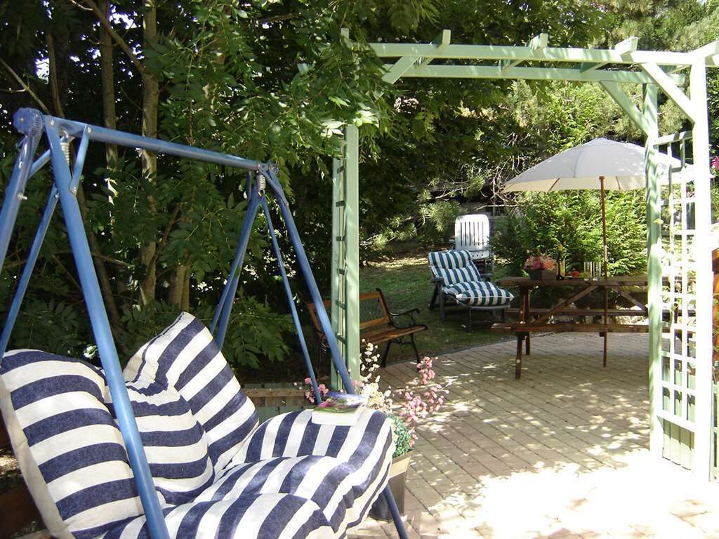 Une terrasse de jardin avec un fauteuil suspendu, un banc et une table avec des chaises.