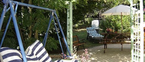 Une terrasse de jardin avec un fauteuil suspendu, un banc et une table avec des chaises.