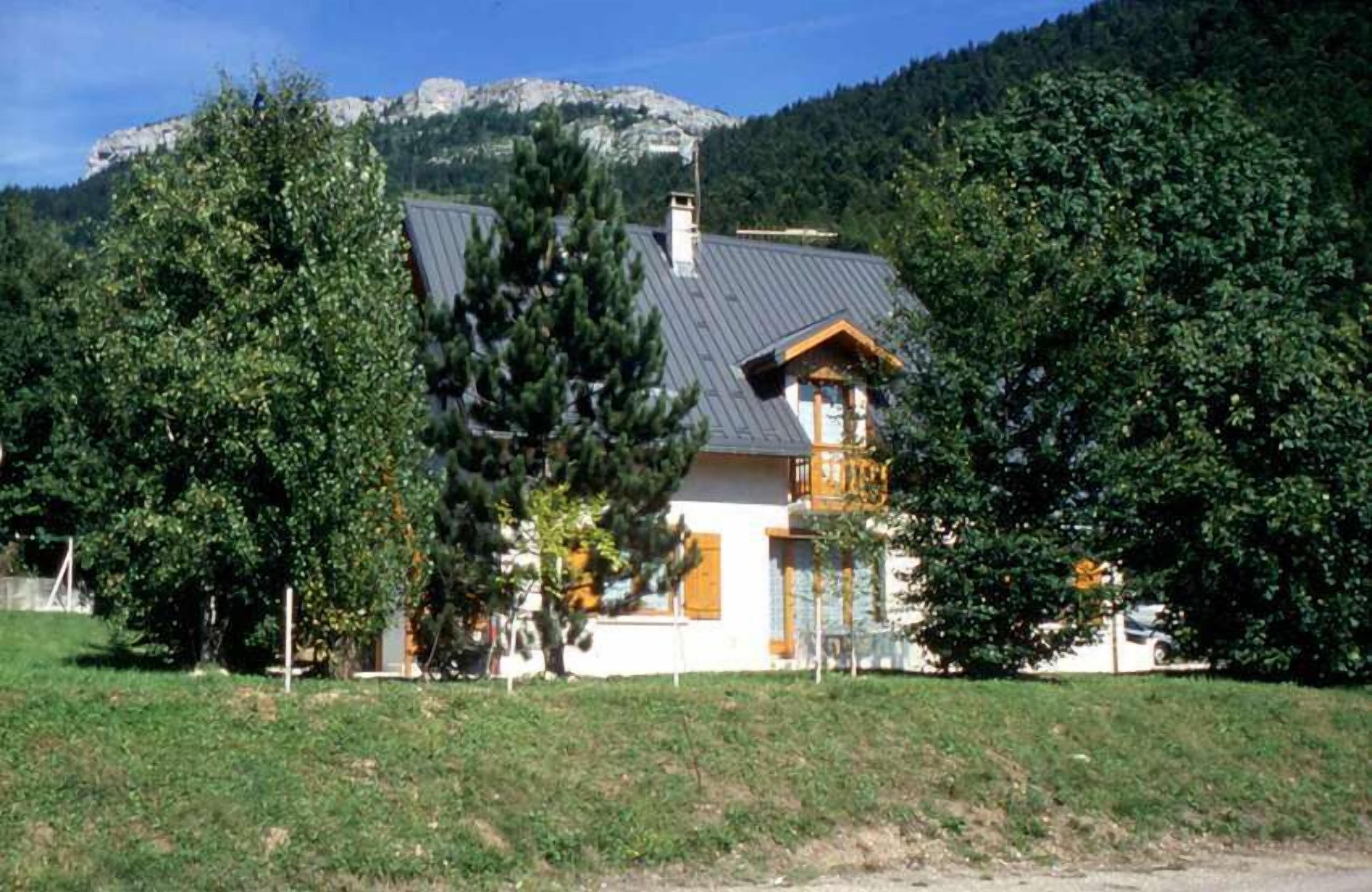 Una casa con techo inclinado, rodeada de árboles y una montaña al fondo.