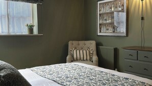 A bedroom with a bed, a chair, a dresser, a radiator, and a wall-mounted shelf with bottles. - Skylarks (Winchester)