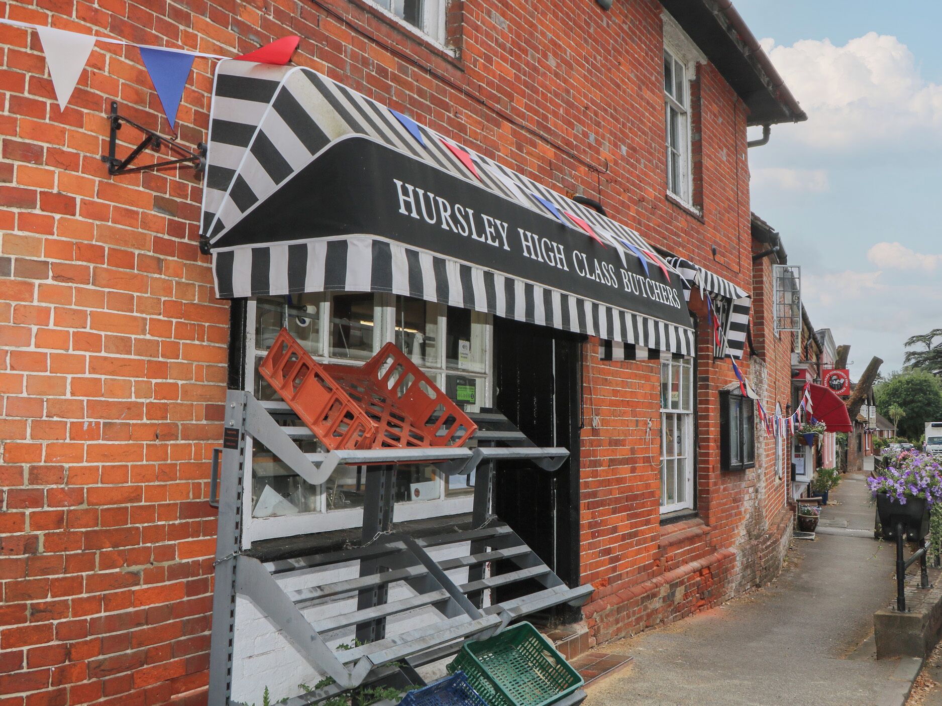 A brick building with a black and white striped awning and a sign that reads 'Hursley High Class Butchers.'