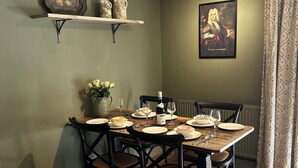 A dining area with a table set for four, chairs, a wine bottle, and a painting on the wall. - Skylarks (Winchester)