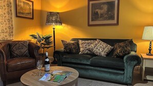 A living room with a leather sofa, a green sofa with patterned cushions, a round wooden coffee table with a wine bottle and glass, and two wall-mounted lamps. - Skylarks (Winchester)
