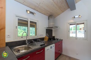 A modern kitchen with a stainless steel sink, red cabinets, and two windows with built-in lighting. - L'Orchis - VALJOUFFREY (VALJOUFFREY)