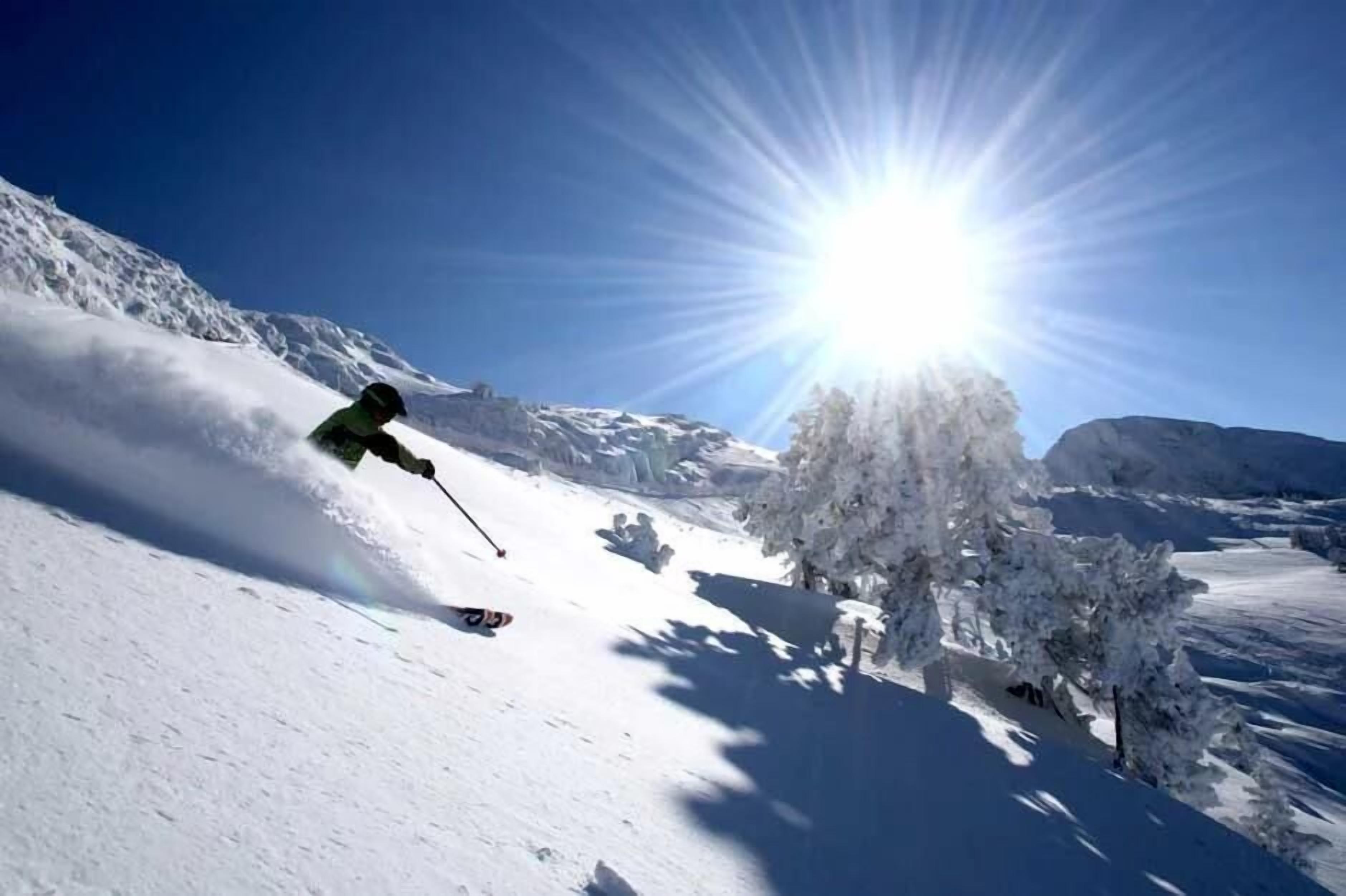 Ein verschneiter Berghang mit einem sich bewegenden Skifahrer, blauem Himmel und strahlender Sonne.