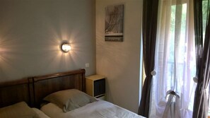 A bedroom with a bed, a bedside table, a wall-mounted light, and a window with curtains. - Les Larmouizes - CRETS IN BELLEDONNE (CRETS EN BELLEDONNE)