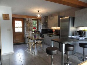 A modern kitchen with a central island, bar stools, a stone accent wall, and a hanging light fixture. - Les Larmouizes - CRETS IN BELLEDONNE (CRETS EN BELLEDONNE)