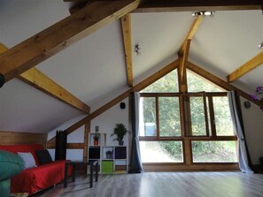 A room with a sloped ceiling, wooden beams, a large window, a red sofa, and a small table with a plant. - Les Larmouizes - CRETS IN BELLEDONNE (CRETS EN BELLEDONNE)