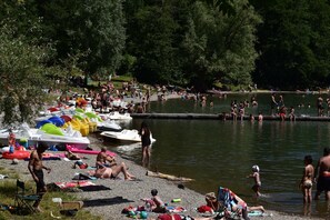 A lakeside area with boats, people swimming, and a grassy area with chairs and umbrellas.