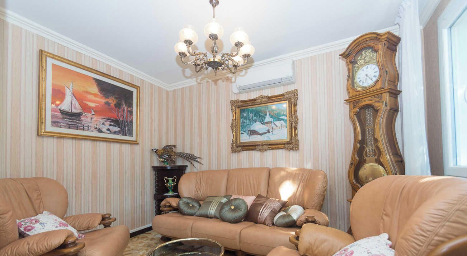 Een kamer met een bank, een grote klok en twee kunstwerken.