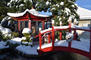 A red bridge over a water feature with a snow-covered gazebo in the background.