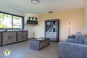 A modern living room with a grey sofa, a coffee table, a TV mounted on the wall, and a bookshelf.