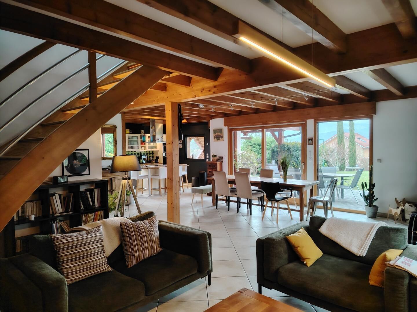 A spacious living area with a high ceiling, wooden beams, a dining area with chairs, and a view of the outdoors through large windows.
