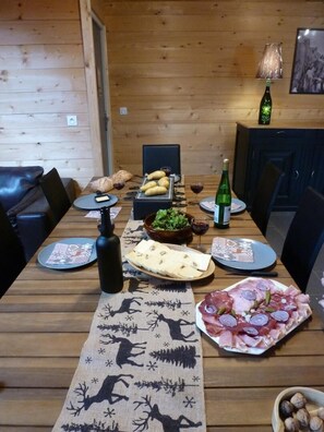 A wooden dining table set with plates, a bottle, and a bowl of food. - Marameille Chalet (ALLEVARD)