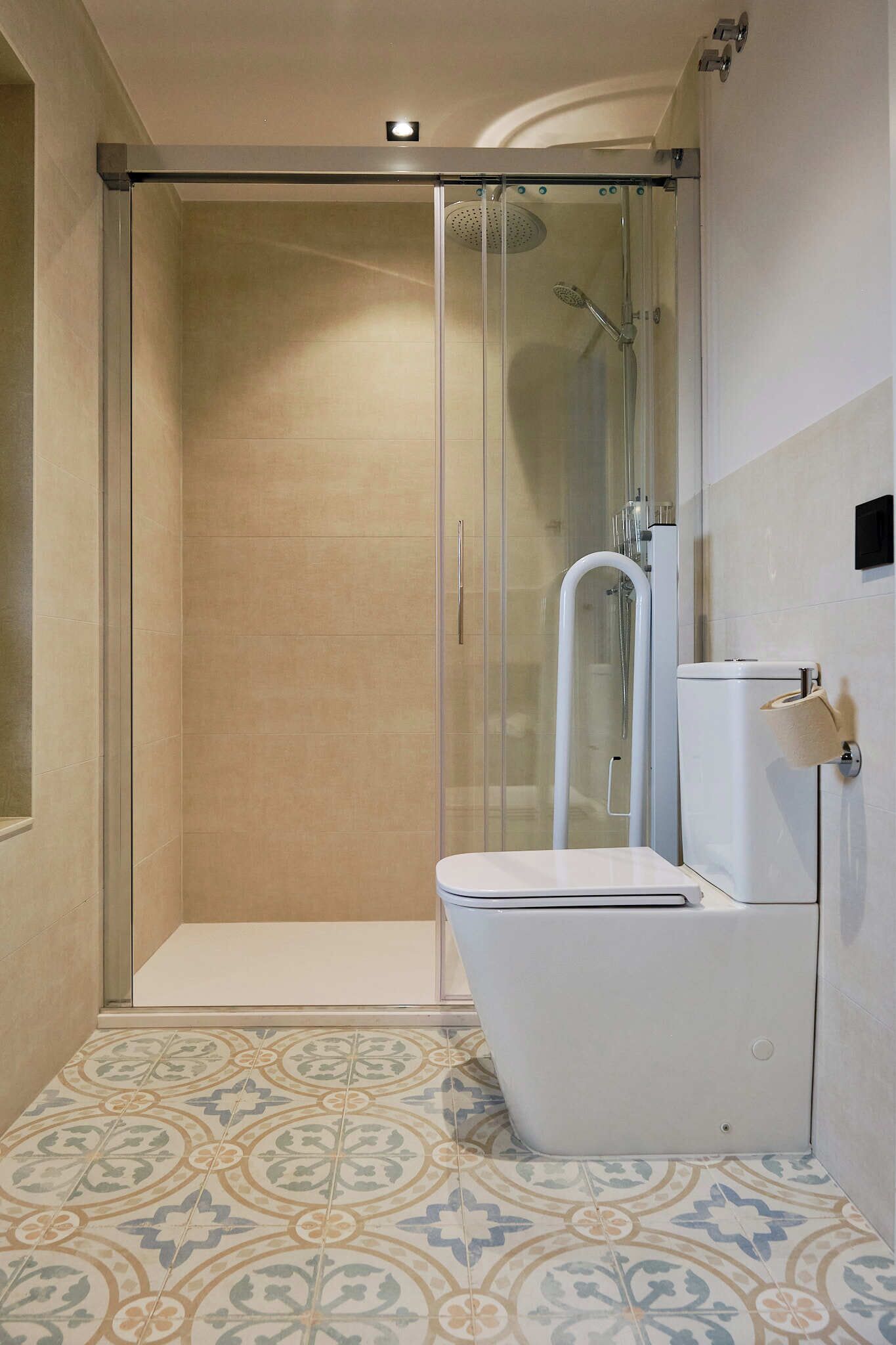Un baño con cabina de ducha, inodoro y suelo de baldosas estampadas.