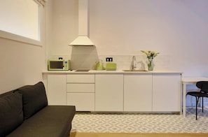 A compact kitchen with a microwave, kettle, toaster, and sink. There's a small dining table with a chair and a sofa in the living area.