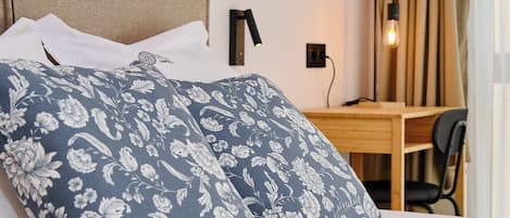 Habitación de hotel con cama, escritorio, silla, lámpara y ventana con cortinas.