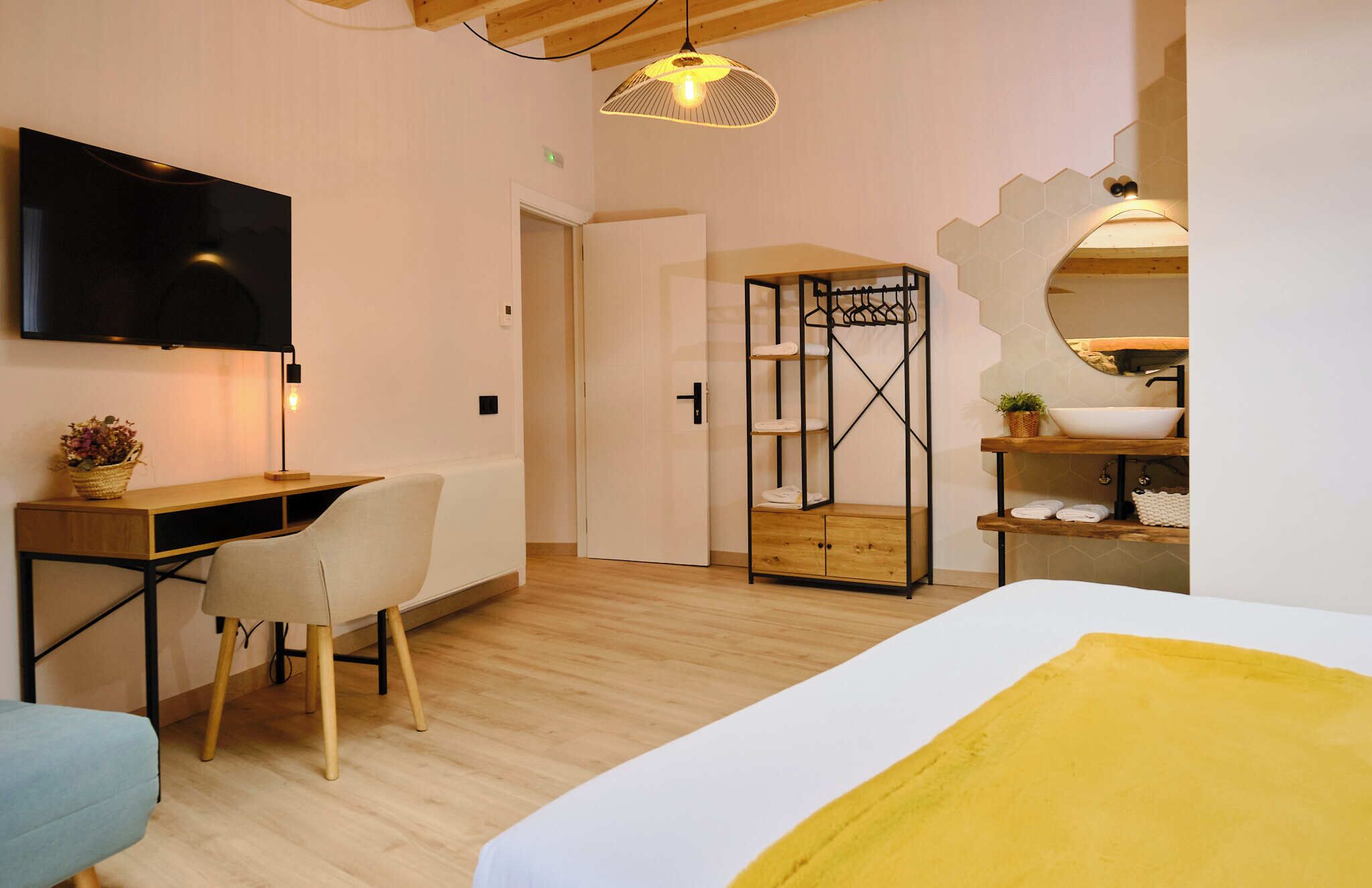 Hotelkamer met een bed, bureau, stoel, televisie, kast en een badkamer met wastafel en spiegel.