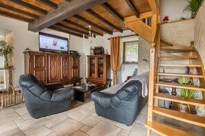 A living room with a wooden staircase, leather sofas, a television, and a bookshelf. - L'Écoline 5-Star Vacation Rental (BRION)