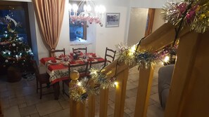 A dining area with a table set for four, a Christmas tree, and a staircase with festive garlands. - L'Écoline 5-Star Vacation Rental (BRION)