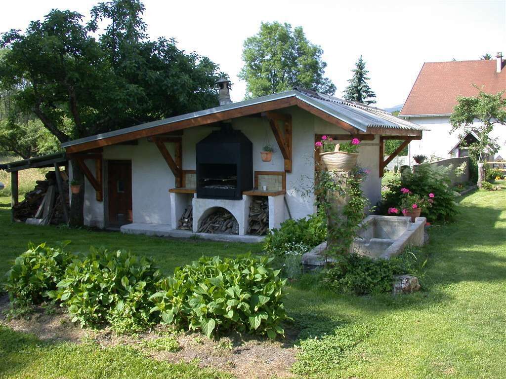 A rustic cabin with a chimney, a wooden porch, and a garden with green plants and flowers.