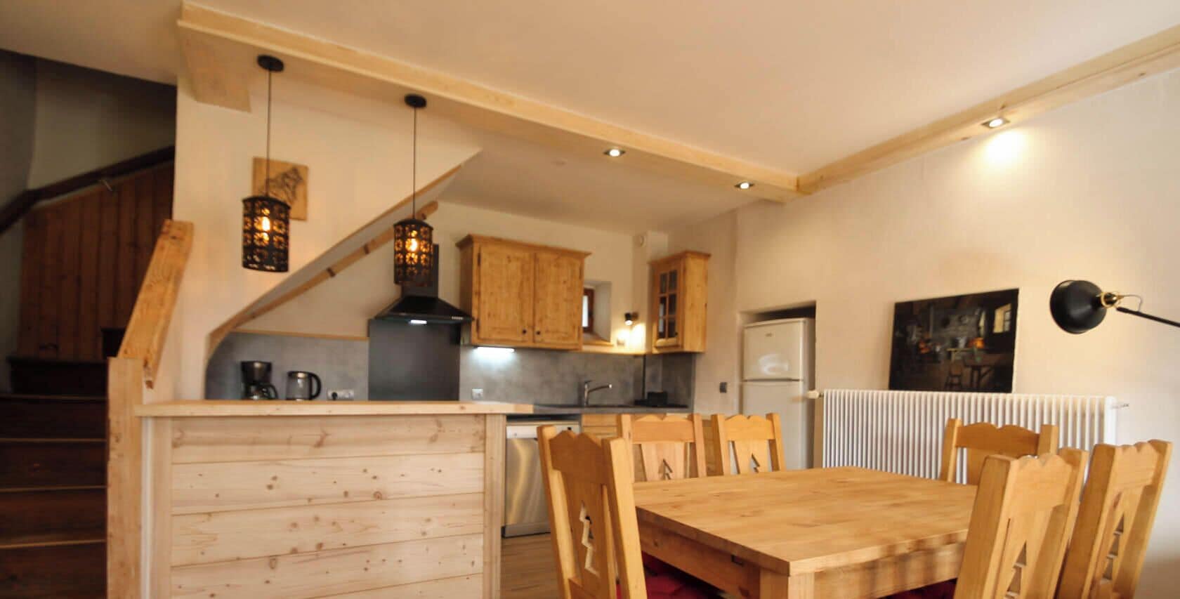Une cuisine avec des meubles de rangement en bois, une table à manger avec des chaises et un escalier avec des rampes en bois.