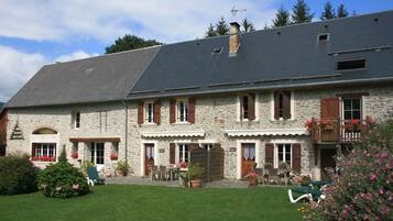 A stone building with a sloped roof, multiple windows with shutters, and a small balcony.