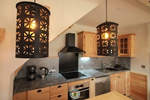 Una cocina moderna con armarios de madera, una campana extractora negra, horno empotrado y dos lámparas colgantes con diseños geométricos.