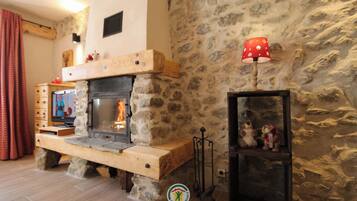 Una chimenea de piedra con un televisor sobre un soporte de madera, una lámpara roja y un estante con peluches.
