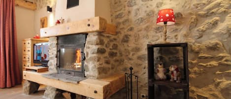 Une cheminée en pierre avec un téléviseur posé sur un meuble en bois, une lampe rouge et une étagère avec des peluches.